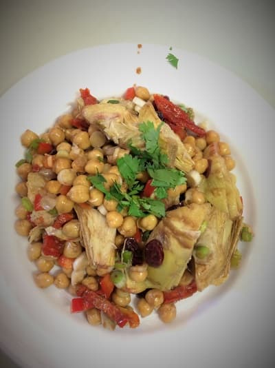 Chickpea and artichoke salad with red pepper and cilantro on a white plate.