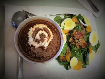 Bowl of roasted red pepper soup beside a spinach salad with mandarin and bacon.