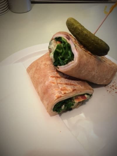 A pressed wrap cut in half on a plate with a dill pickle on top.