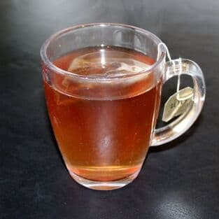 A glass mug of loose-leaf tea steeping on a dark counter.